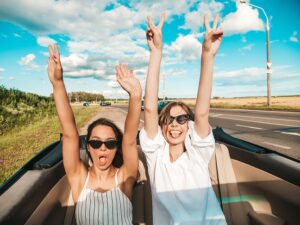 2 Frauen fahren im Oldtimer-Cabrio Hände nach oben gestreckt